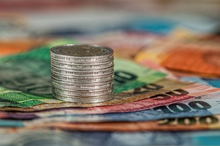 things that drain your wealth-Stack of coins balanced atop a pile of colorful banknotes