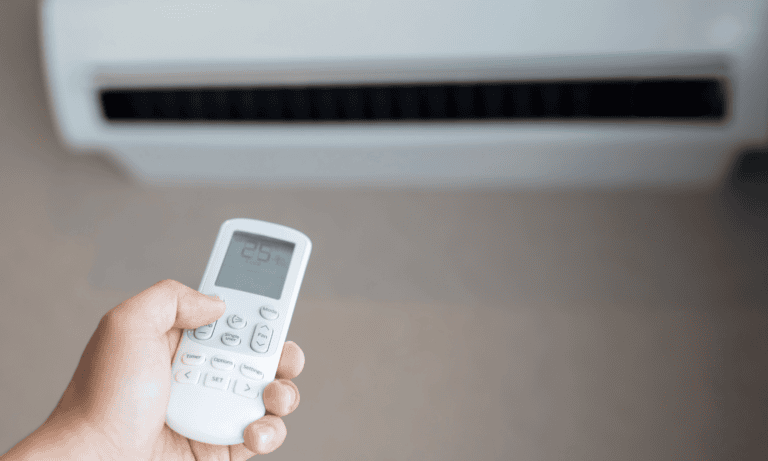 Hand pointing a remote at an air conditioner unit on the wall