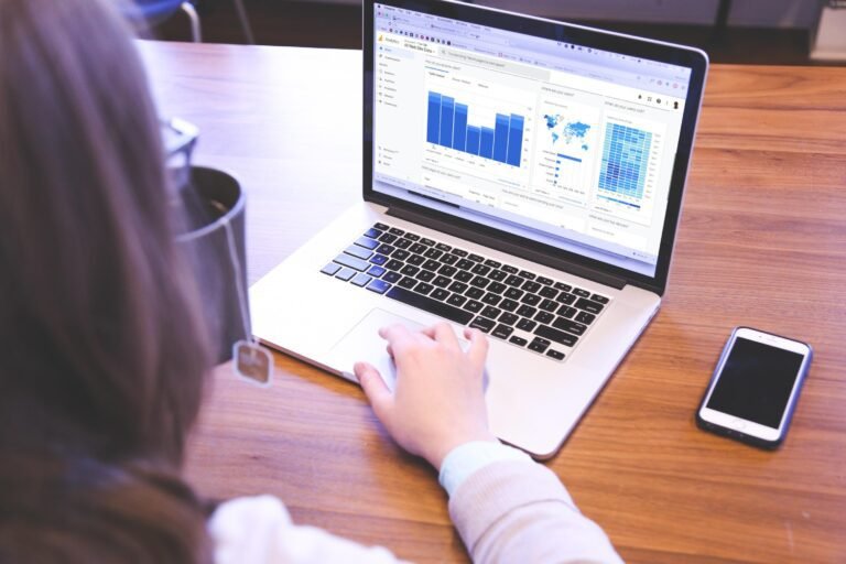 Focused woman analyzing income data charts on a laptop at a wooden desk